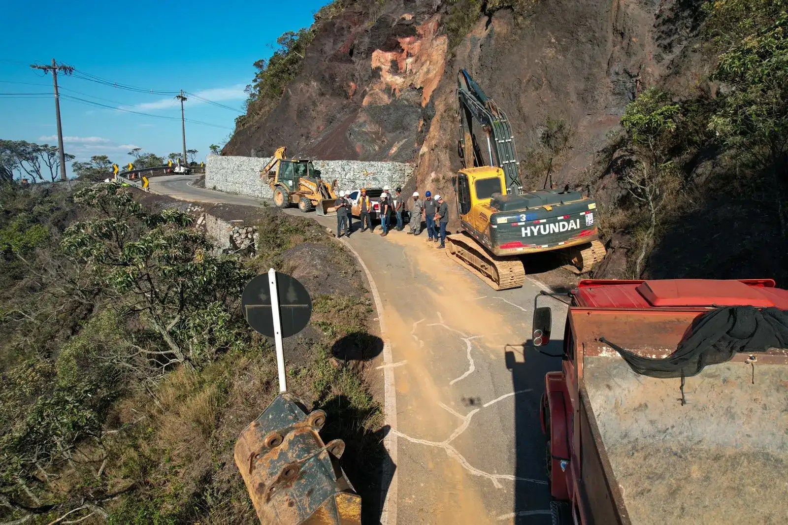 Estrada de serra com escavadeira Hyundai e caminhões em operação